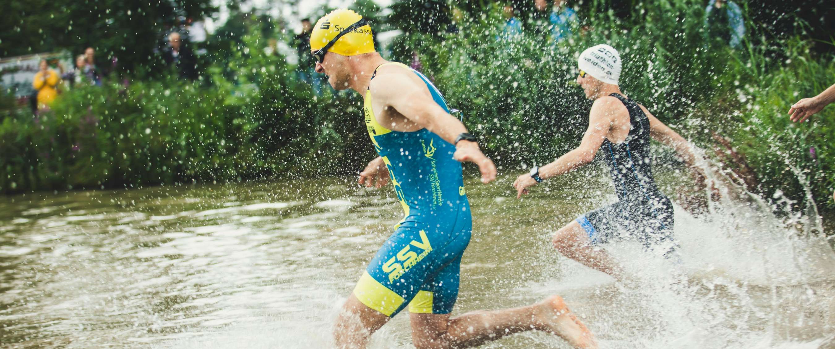 Twee triatleten rennen uit het water aan het einde van het zwemonderdeel.