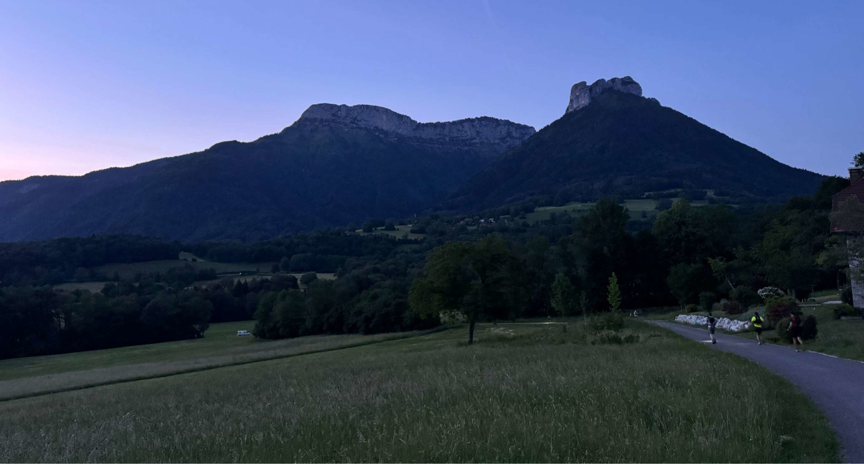 Trois coureurs avancent sur une route dans un paysage montagneux au crépuscule.