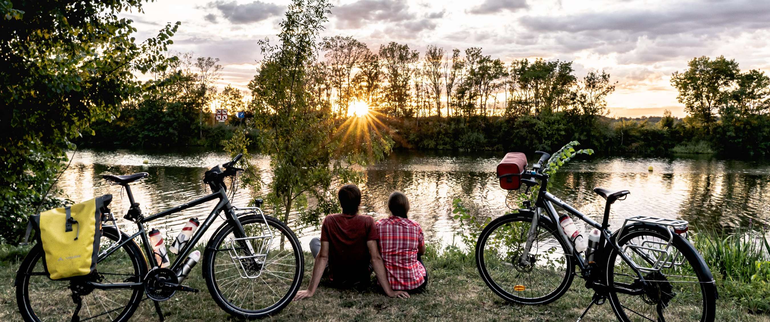 Twee fietsen staan aan de waterkant terwijl twee personen naar de zonsondergang kijken.