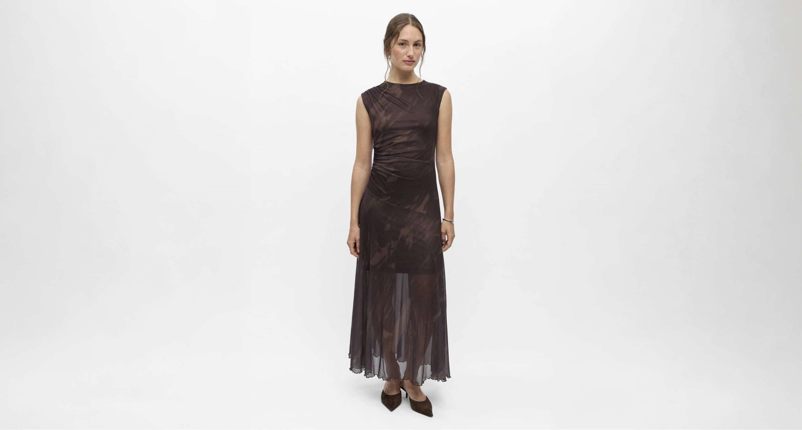 Robe longue brun foncé à silhouette ajustée et tissu transparent à partir des genoux.