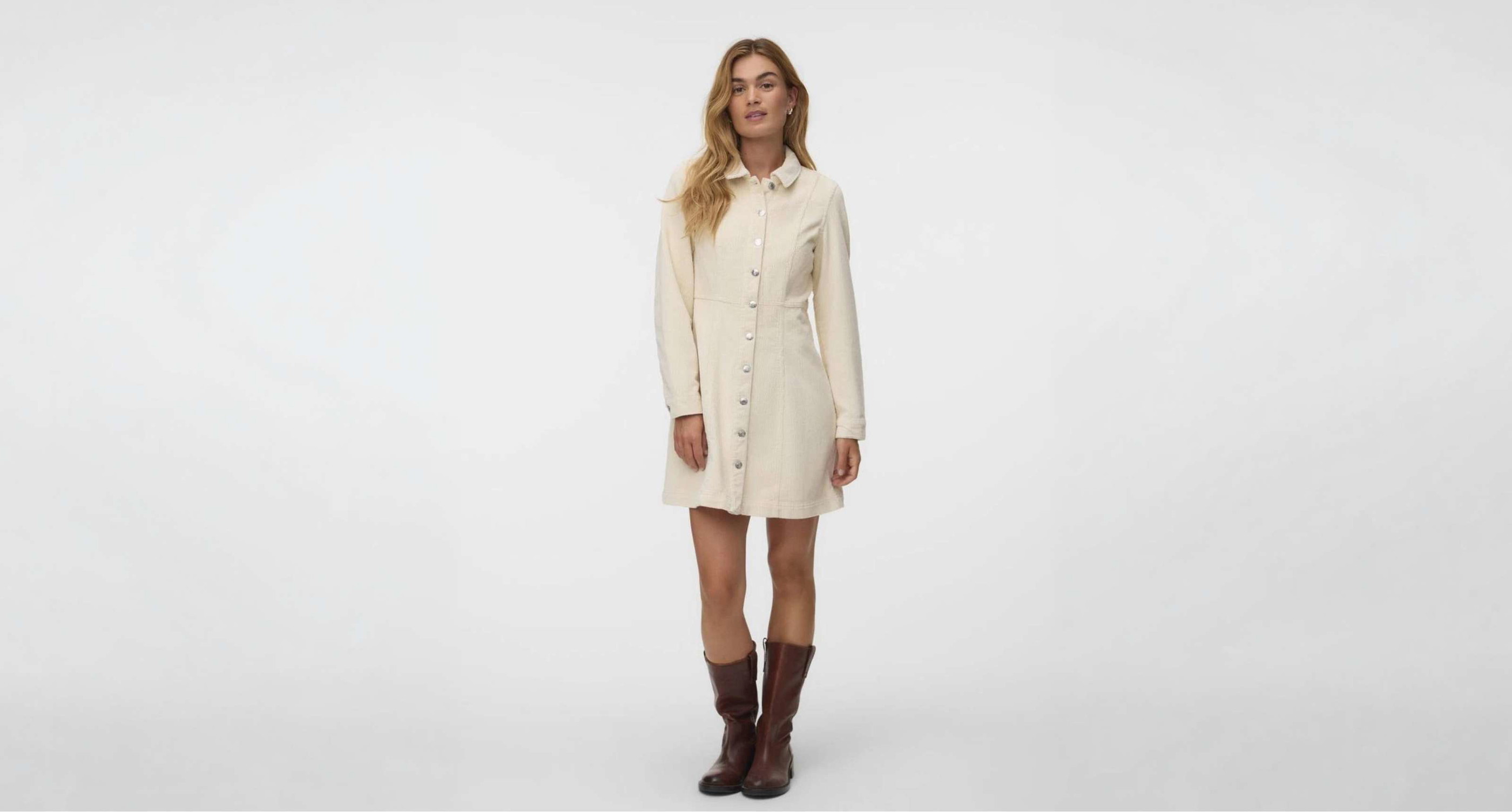 Une personne porte une mini-robe crème à manches longues, col et boutons sur le devant.