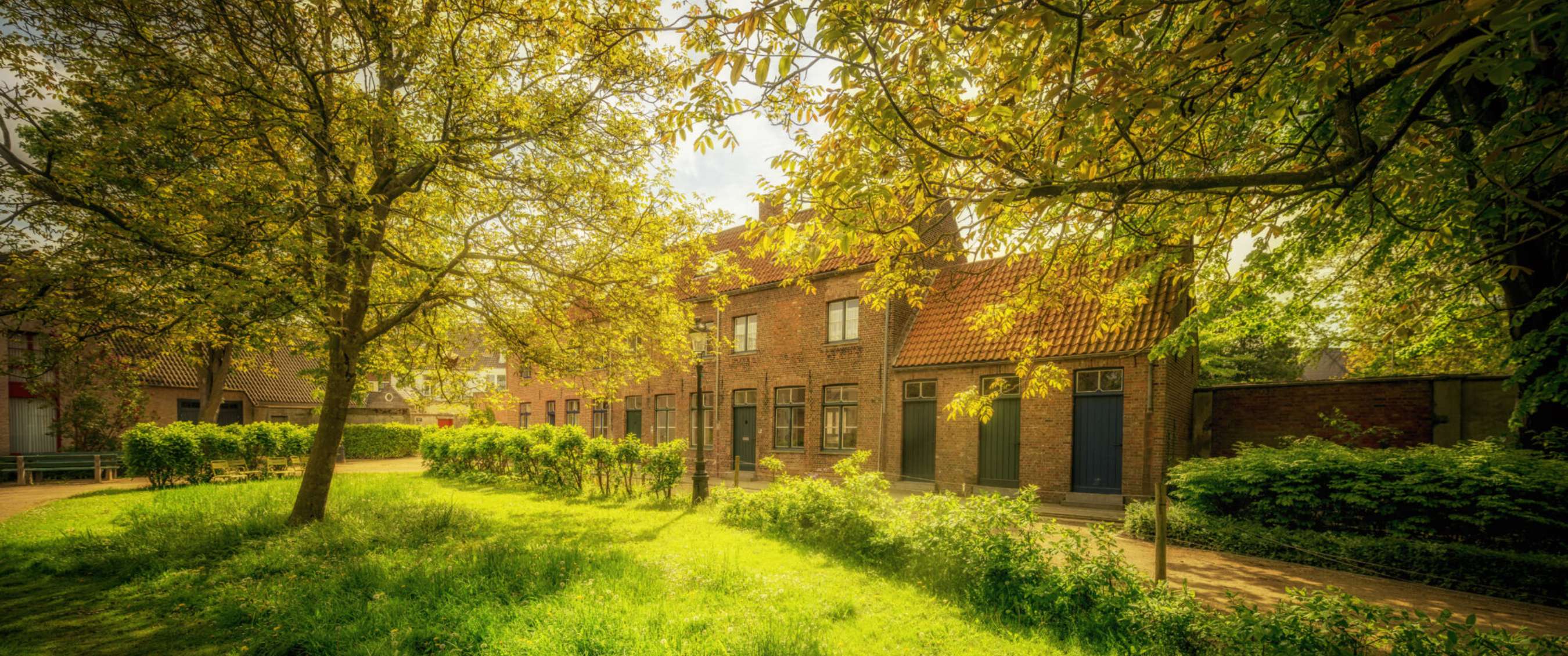 Lumière du soleil sur des maisons en briques autour d’une cour verdoyante à Bruges.