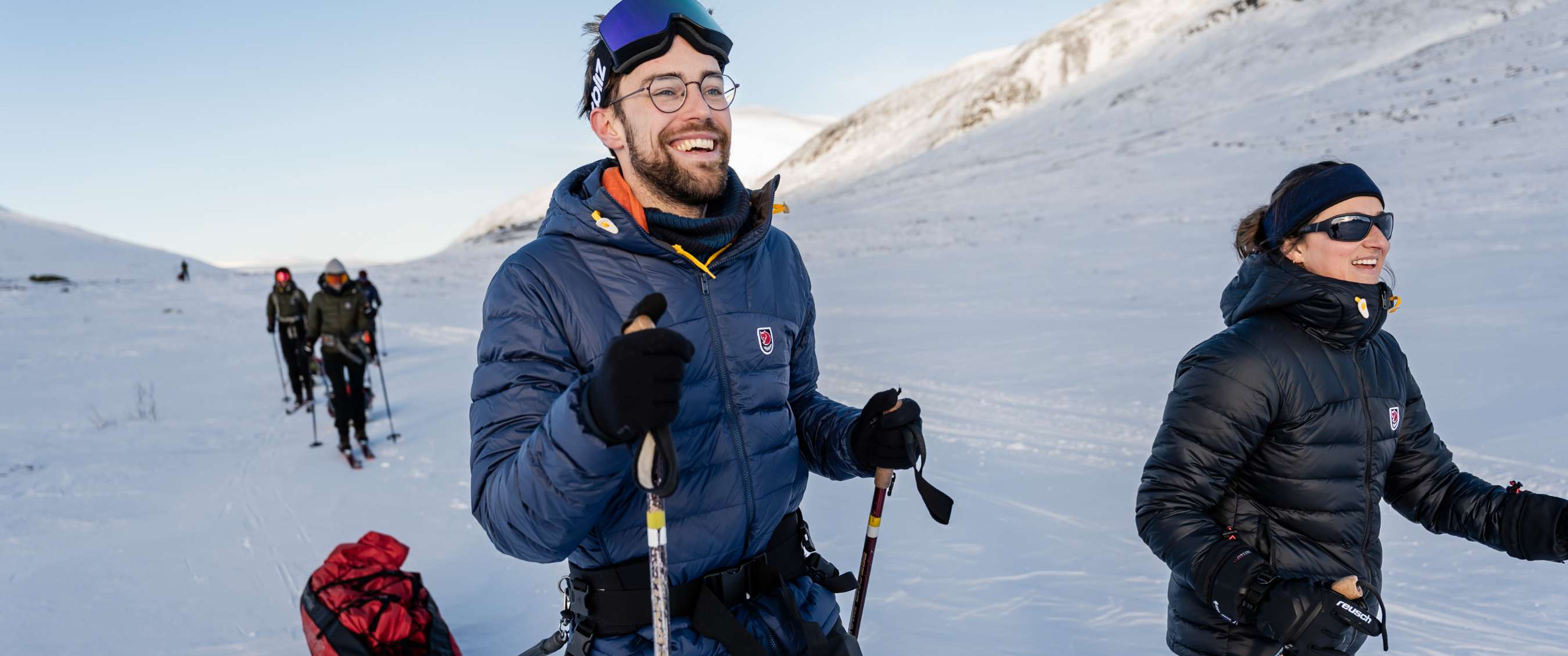 Un homme et une femme en vestes matelassées font du ski de fond dans un paysage montagneux enneigé.
