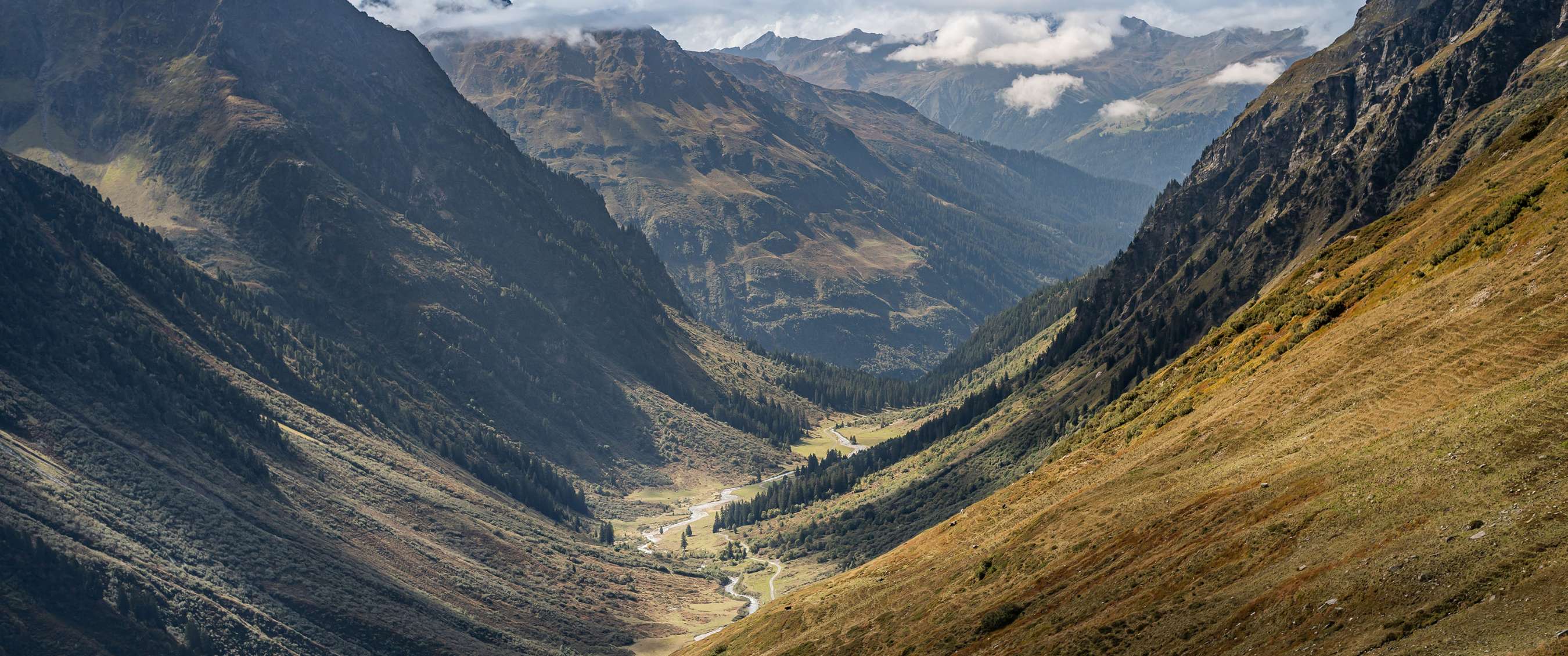 Uitzicht op een brede bergvallei met een kronkelende rivier.