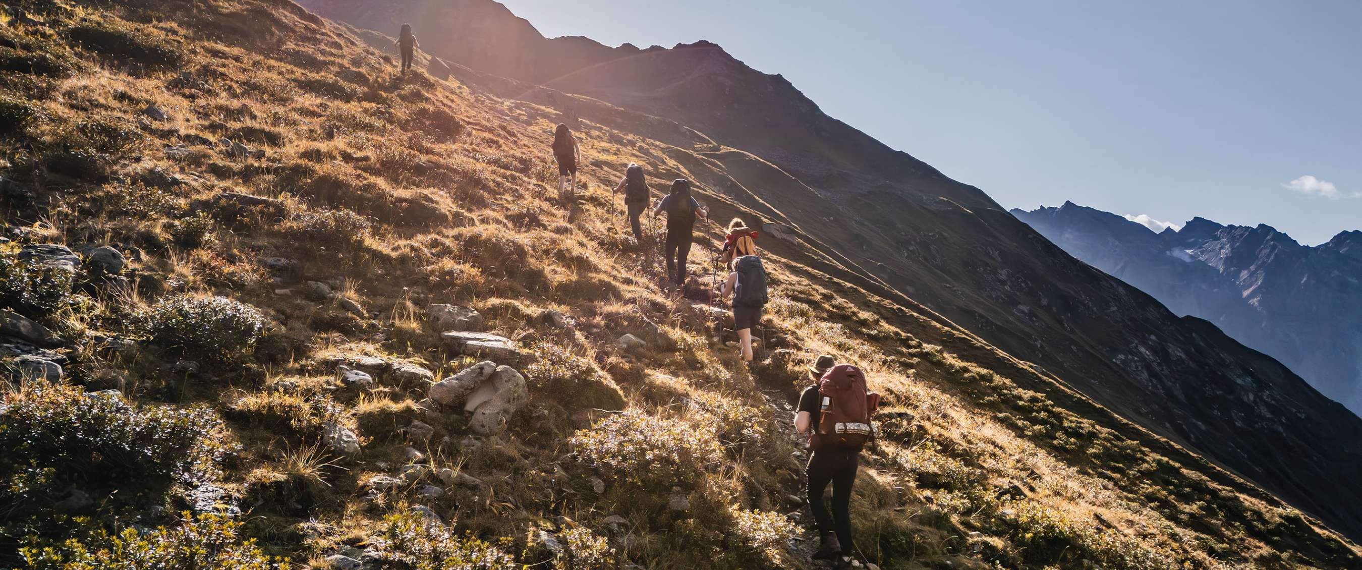 Wandelaars lopen in een rij omhoog op een zonnige berghelling.