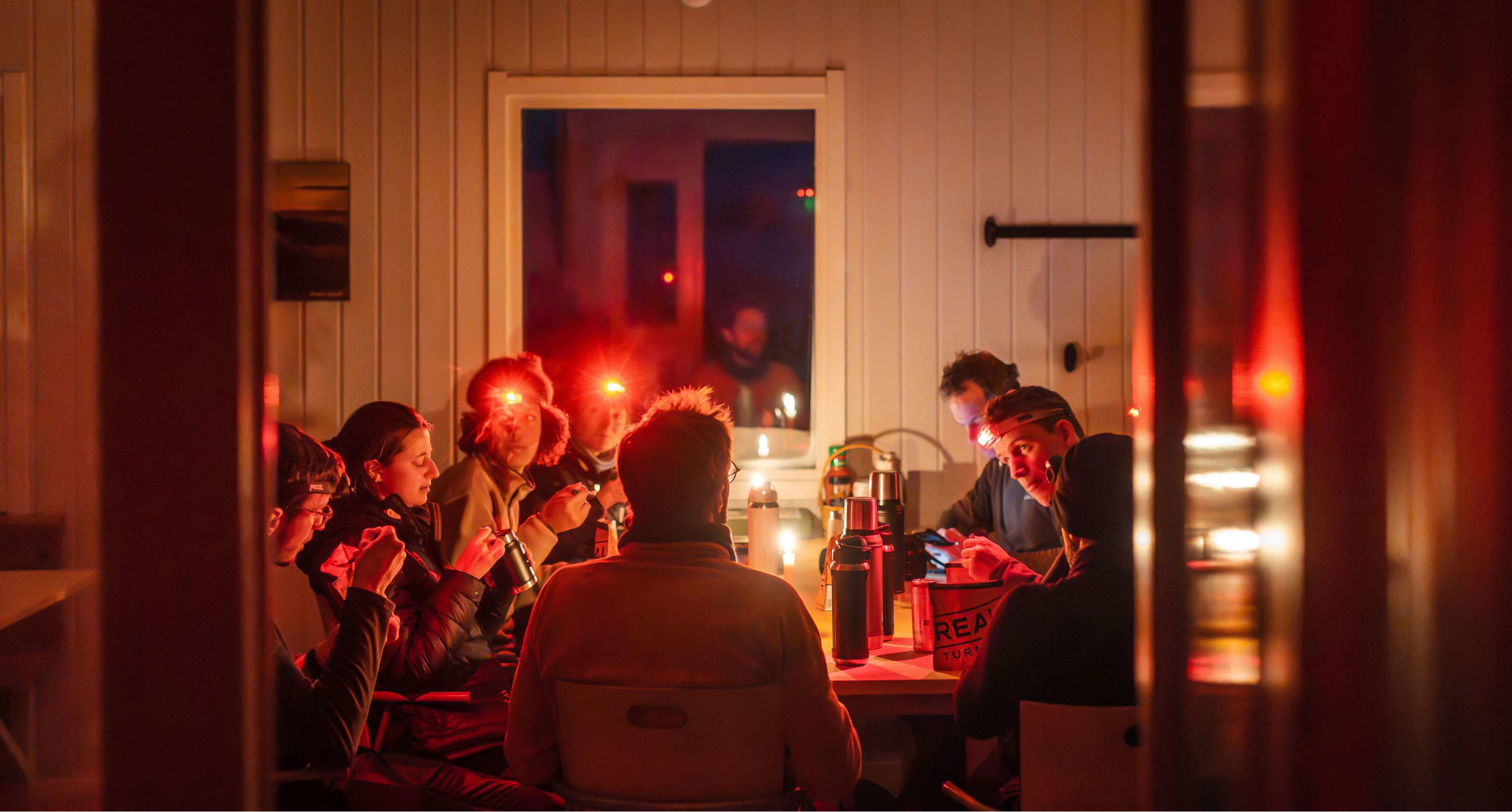 Groep mensen met hoofdlampen eet samen aan een tafel in een warm verlichte houten ruimte.