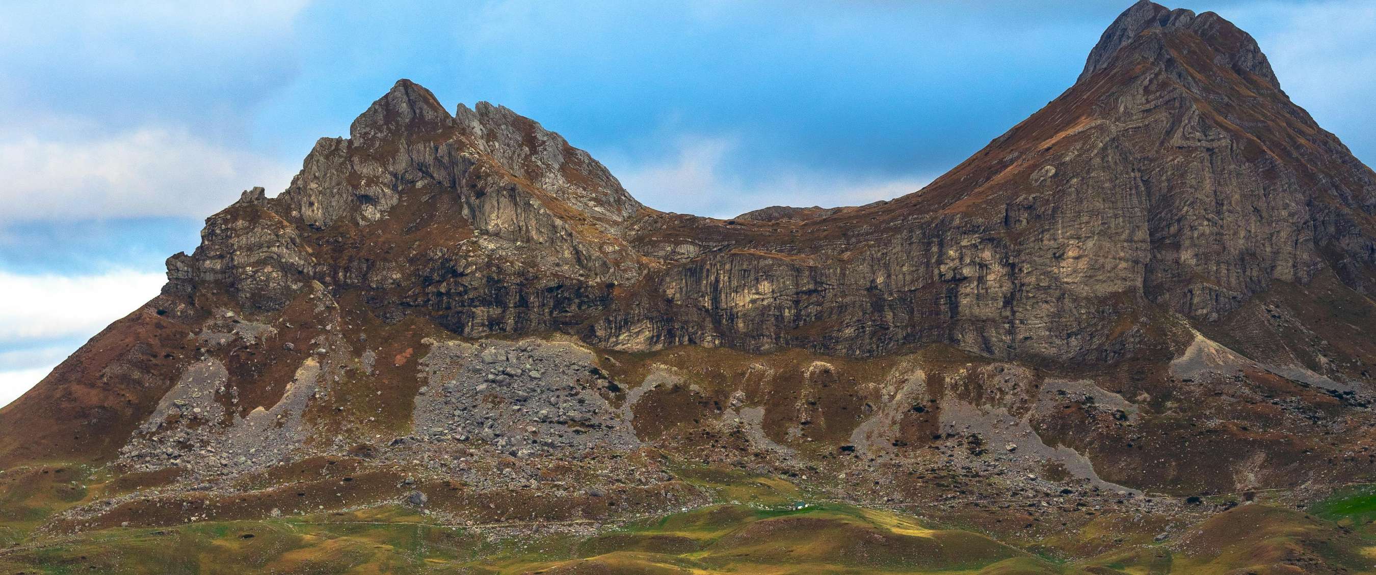 Rotsachtige bergketen met steile pieken en kale hellingen onder een blauwe lucht.