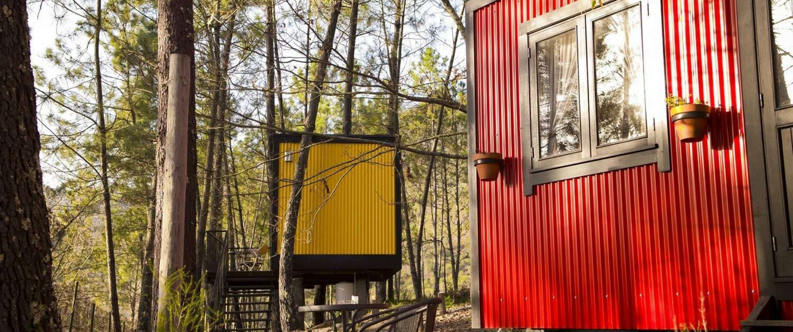 Cabanes compactes sur pilotis dans un environnement boisé, aux parois extérieures rouges et jaunes.