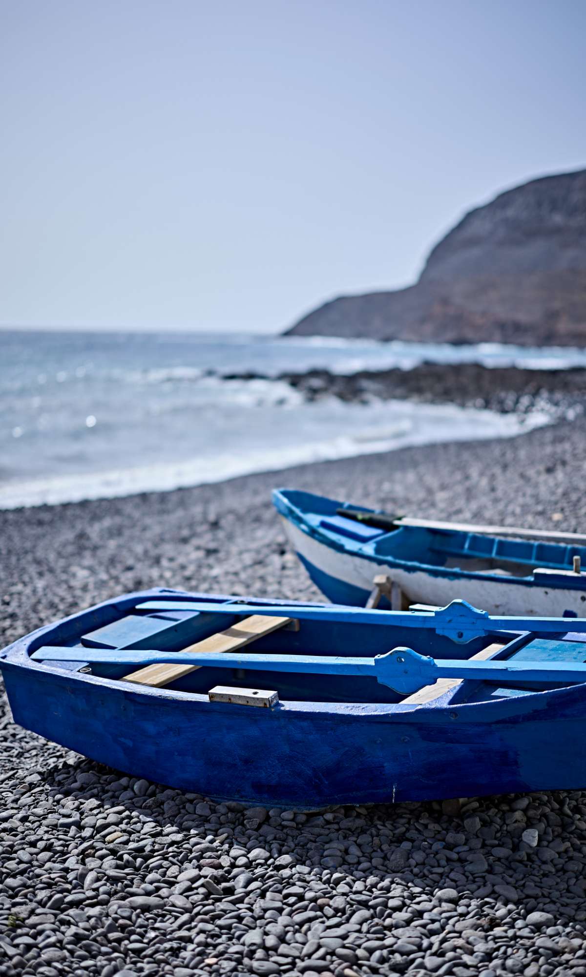 Bateau bleu avec rames sur une plage de galets au bord de la mer.