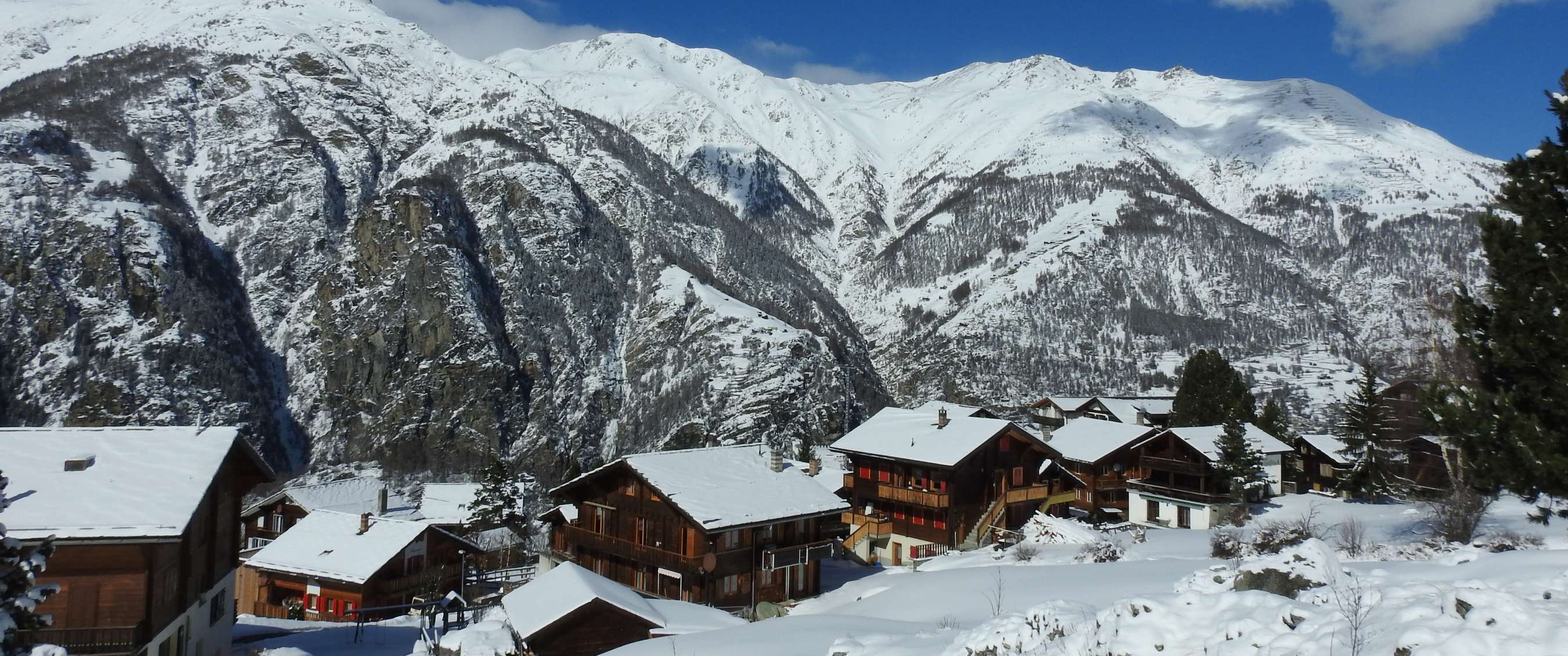 Bergdorp met houten chalets onder steile besneeuwde bergwanden.