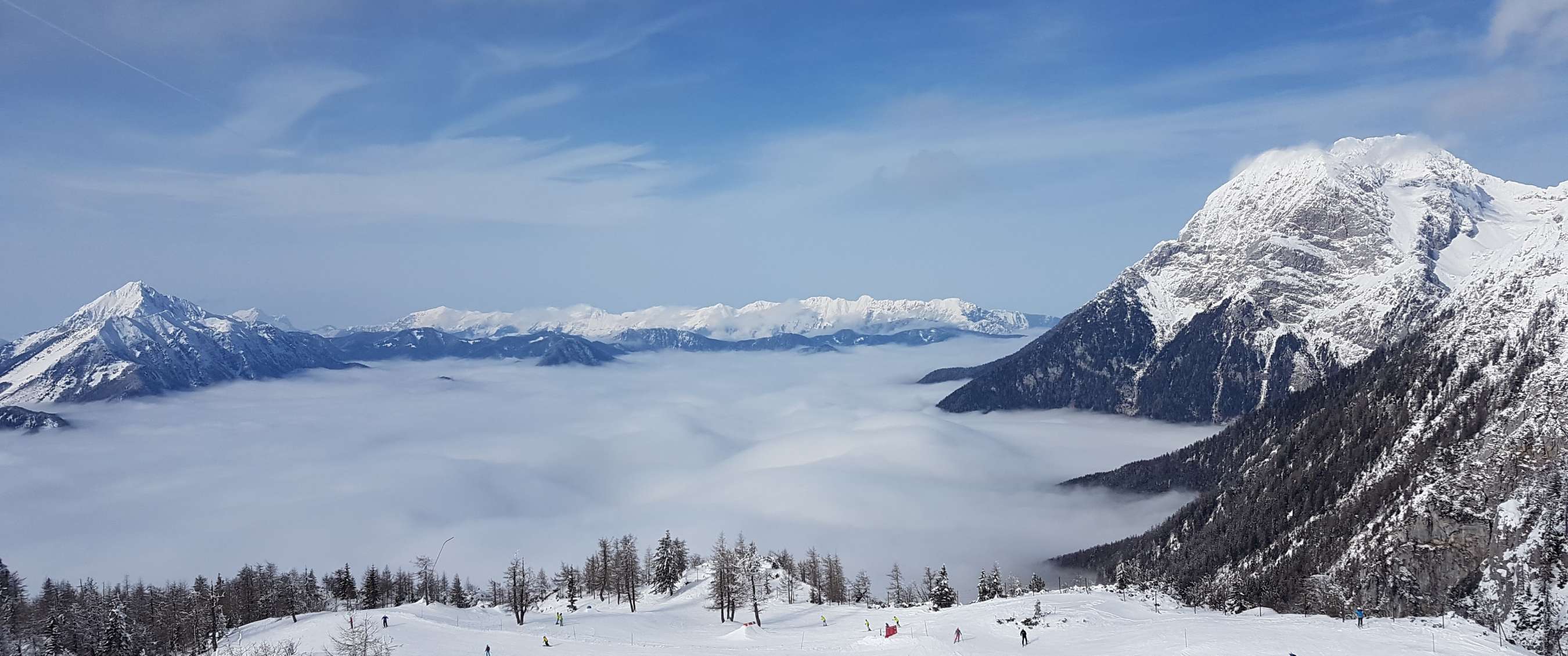 Des skieurs sur une piste avec vue sur des sommets de montagne enneigés qui dépassent des nuages à Krvavec.