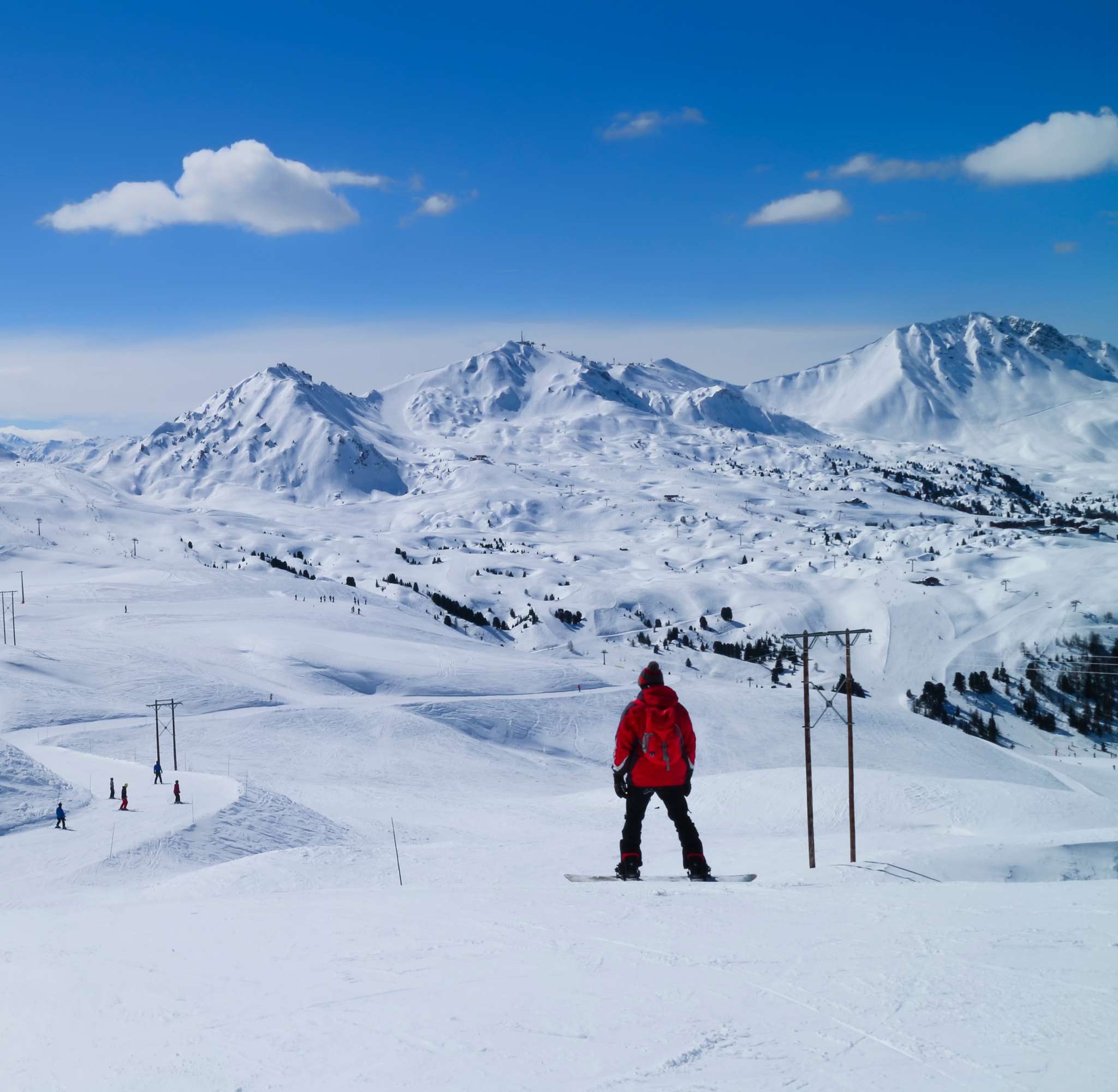 Un snowboarder en veste rouge sur une pente enneigée, avec vue sur un vaste paysage de montagne à La Plagne.