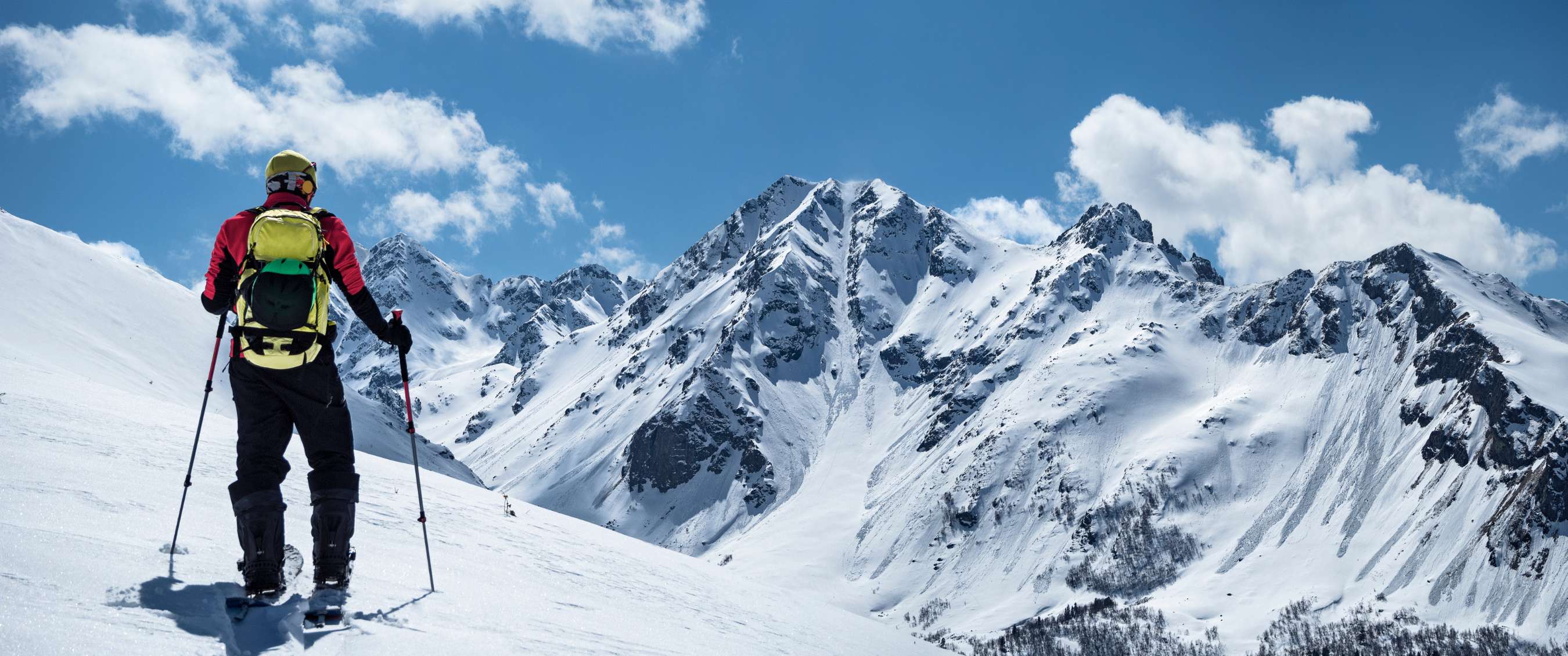 Een skiër kijkt uit over besneeuwde bergpieken onder een heldere blauwe lucht.