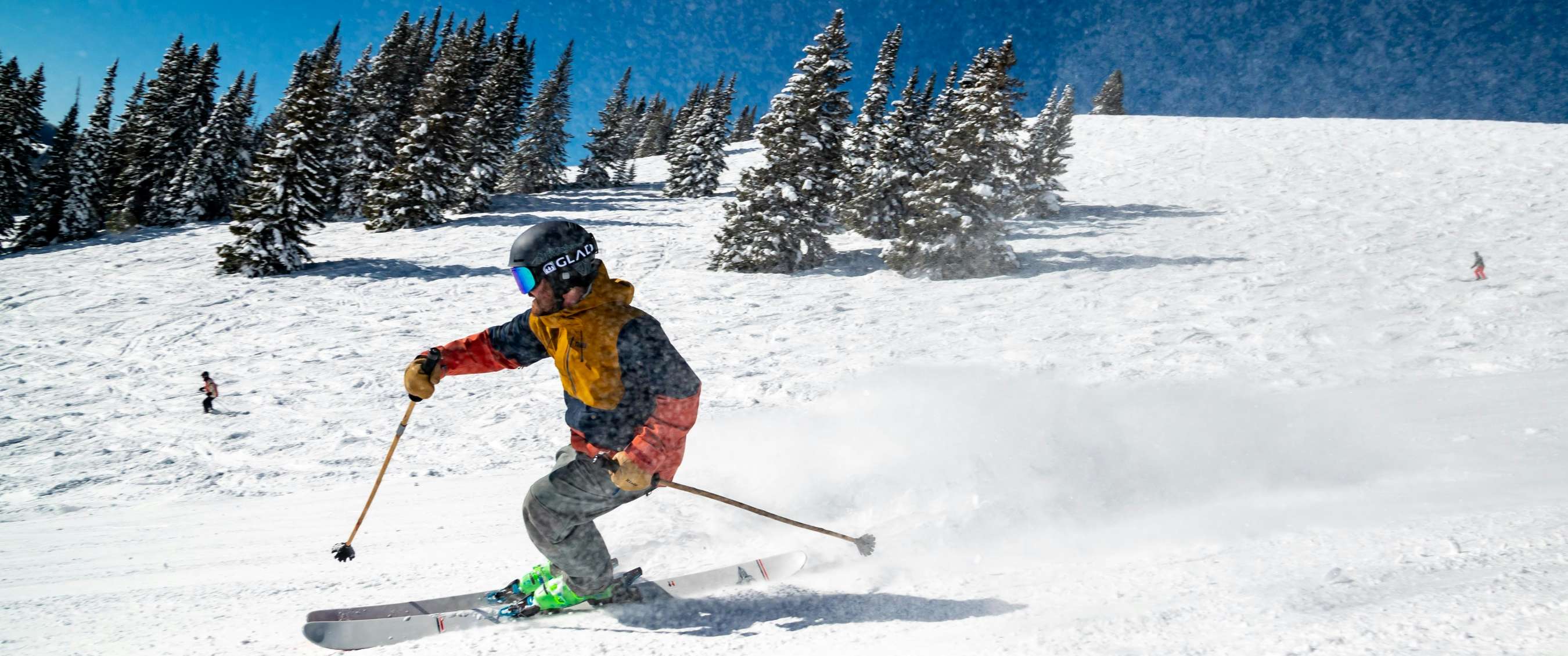 Persoon op ski’s die sneeuw opspuit tijdens een snelle afdaling op een zonnige piste.