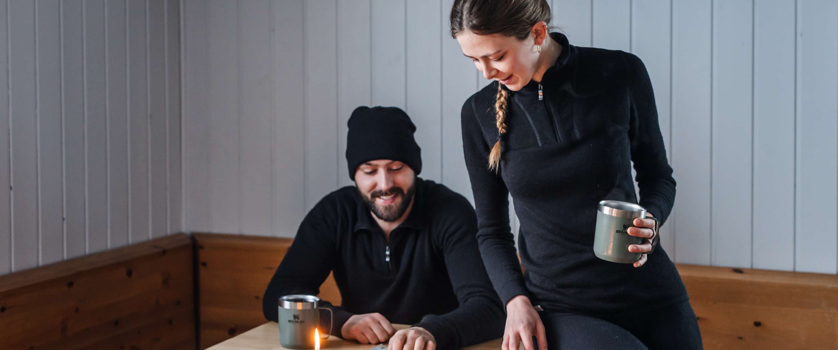 Deux personnes en vêtements thermiques noirs regardent un magazine à la lueur des bougies.